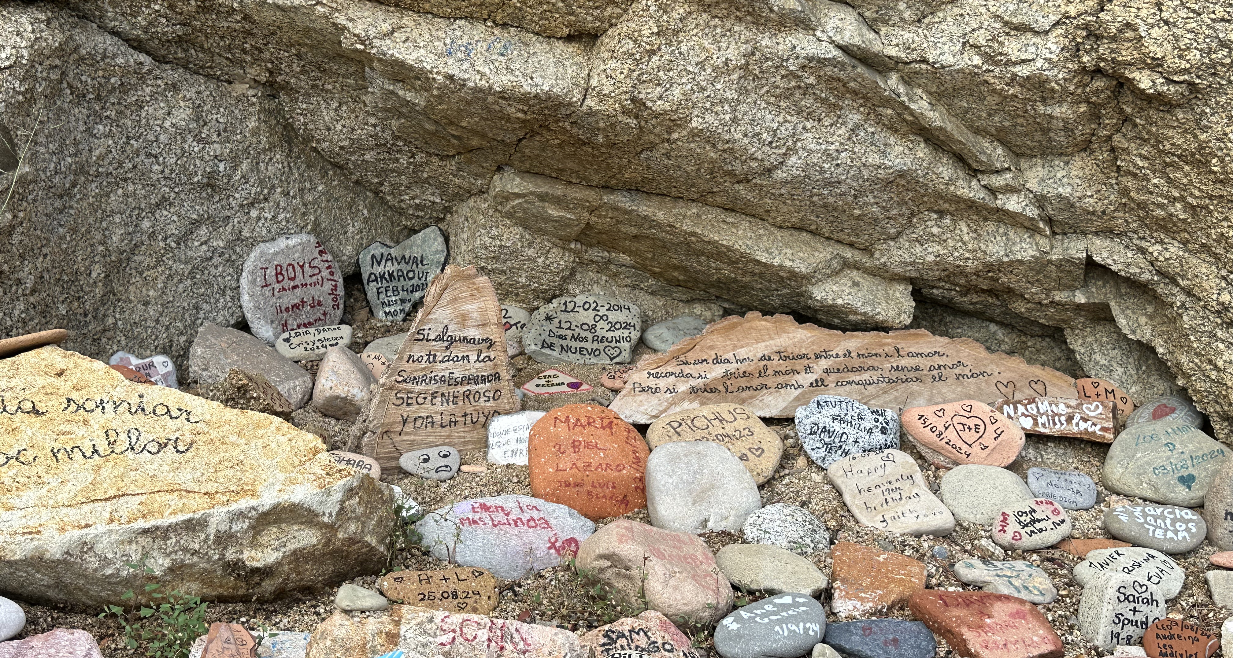 La imagen muestra un conjunto de piedras pintadas y escritas por diversas personas que las han dejado junto a una roca del paseo marítimo de Lloret de Mar como recuerdo de su estancia o de sus vacaciones.